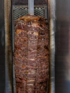 Close-up of a traditional doner kebab on rotisserie, showcasing grilled meat's texture and flavor.